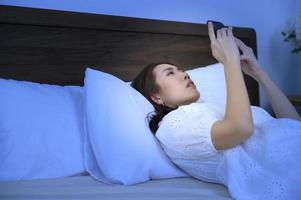 asiatisk kvinna känsla öga anstränga Trötthet medan använder sig av smartphone i sovrum foto
