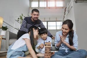 glad asiatisk härlig thailändsk familjeaktivitet, föräldrar, pappa, mamma och barn har roligt att leka och glada träleksaksblock tillsammans på vardagsrumsgolvet, fritidshelger och livsstil för hemligt välbefinnande. foto