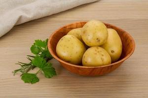 rå potatisar i en skål på trä- bakgrund foto
