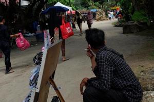 lampung, indonesien - Maj 6, 2022, en leksak -handlare är hukande medan rökning i de marknadsföra foto