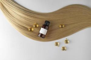 en hår vård olja eller serum i gyllene kapslar liggande på en strå av blond hår, produkt marknadsföring mockup. en begrepp av hår vård i en salong eller på Hem foto