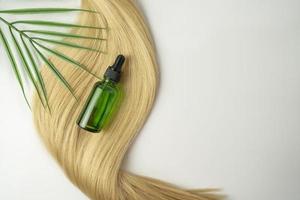 en naturlig olja eller serum för hår vård liggande på en lager av blond hår foto