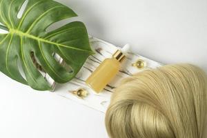 en naturlig grundläggande olja eller serum för hår vård liggande på en vit trä- bricka. hår vård och glättning begrepp foto