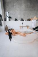 avslappnad lady tar bad, njuter och avkopplande medan liggande i badkar foto