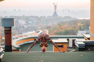 kvinna håller på med yoga på de tak av en skyskrapa i stor stad. foto