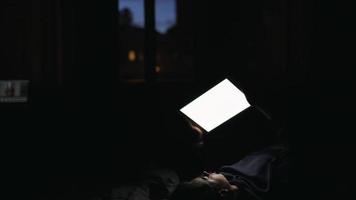 närbild. en ung kvinna är skriver på en läsplatta. liggande i säng. på natt foto