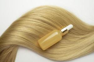 en skönhet serum med vitamin c eller glättning olja för hår vård liggande på de strå av blond hår foto