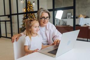 barn och mormor ser på de kamera med bärbar dator foto