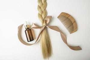 en naturlig olja eller serum för hår vård behandling och en hårlock av blond hår med rosett liggande på en vit bakgrund foto