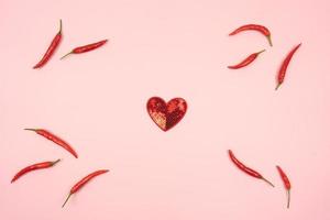 en röd hjärta och röd varm chili paprikor runt om den lögn på en rosa bakgrund foto