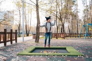 Lycklig skola flicka Hoppar på en små trampolin i de parkera foto