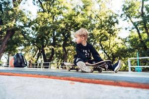 ung unge Sammanträde i de parkera på en skateboard. foto