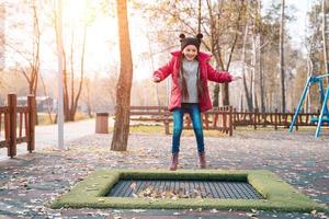 Lycklig skola flicka Hoppar på en små trampolin i de parkera foto