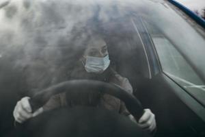 ung kvinna i en mask och handskar körning en bil. foto