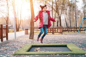 Lycklig skola flicka Hoppar på en små trampolin i de parkera foto