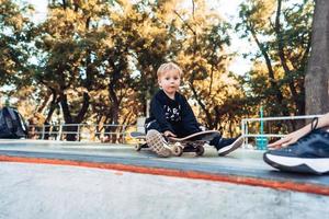 ung unge Sammanträde i de parkera på en skateboard. foto