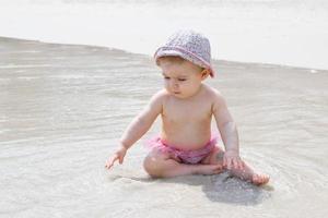 liten bebis flicka är spelar med vatten och sand på strand. sommar semester på hav. foto