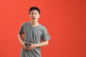 ung asiatisk man bär en vit tshirt sjuk, lidande från magont, smärtsam sjukdom begrepp. foto