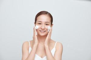 glad asiatisk kvinna kvinna applicering skumning rengöringsmedel, har rena färsk friska hud. foto