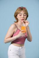asiatisk flicka innehar glas av orange juice i henne vapen och ler Framställ i de studio foto