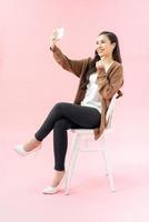 leende ung kvinna framställning selfie Foto på smartphone över rosa bakgrund