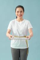 en asiatisk kvinna innehav skalor med en tejp mäta runt om henne mage på en blå bakgrund foto