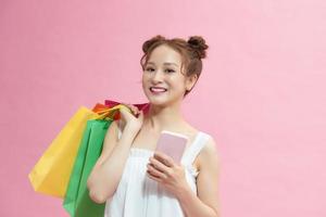 Lycklig kvinna använder sig av smartphone och innehav handla påsar isolerat på rosa foto