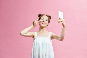 porträtt av en ung attraktiv kvinna framställning selfie Foto på smartphone isolerat på en rosa bakgrund