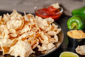 stänga upp hand håll chip dopp tomat salsa med tallrik med taco, nachos pommes frites och tomat dopp. kryddad nachos på rustik trä- bakgrund foto