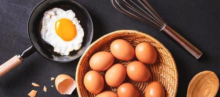 meny matlagning i kök ägg friterad ägg i de panorera och färsk ägg i korgar på svart trä- bakgrund foto