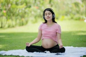 en gravid asiatisk kvinna slappnar av med yoga stretching övningar i de parkera för de hälsa av de mor och de ofödd barn foto