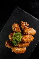 friterad kyckling vingar eller utegrill stänkte med sesam frön på en svart tallrik och placerad på en svart tabell. kryddad och saftig koreanska stil friterad kyckling gata mat foto