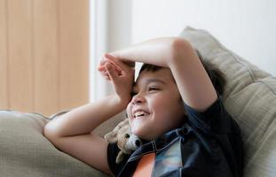 porträtt Lycklig unge skrattande, söt liten pojke med stor leende Sammanträde på soffa har roligt tittar på tecknad serie på tv, positiv barn med leende ansikte avkopplande njut av Lycklig tid ensam på helgen. foto