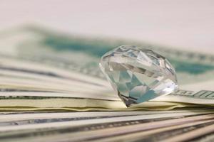 oss pengar räkningar med stor diamant stänga upp. stor belopp av dollar och enorm transparent pärla på tabell. företag och smycke foto