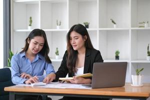 två unga asiatiska affärskvinnor diskuterar med nystartsprojektidépresentation, analyserar planering och finansiell statistik och investeringsmarknaden på kontoret. foto