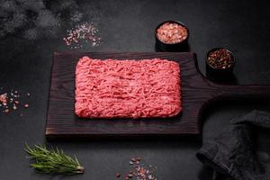 färsk mald nötkött på skärande styrelse på mörk bakgrund med Ingredienser för matlagning foto