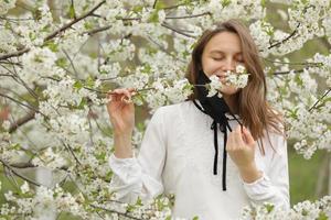 glad vacker flicka tog av sig sin medicinska mask för att andas in blommalukten. en flicka i en mask står i blommor. slutet av karantänen foto