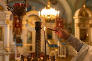 ortodox kyrka. kristendomen. hand av prästen tänder brinnande ljus i traditionell ortodox kyrka på påskafton eller jul. religion tro ber symbol. foto