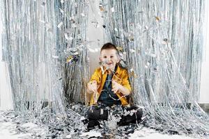 födelsedag fest begrepp. Lycklig pojke stående under faller silver- konfetti, glad emotionell manlig preteen unge har roligt över silver- fest studio bakgrund, kopia Plats foto