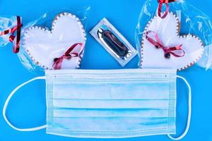 hjärtans dag gåva, erotisk grej, kondom, hjärtformade småkakor och medicinsk mask på en blå bakgrund. skydd begrepp. foto