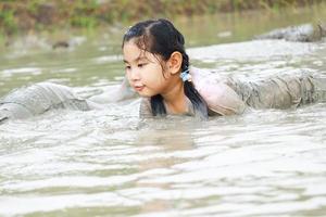 barn har roligt spelar i de lera i de fält på en molnig dag. asiatisk barn vada genom vatten och smutsig lera. barns utomhus- spela och inlärning utanför de klassrum foto