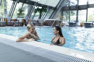 kvinnor vänner talande i slå samman , ha på sig bikini lyx hotell nära strand på tropisk ö koppla av. skön ung kvinnor har roligt i simning slå samman, leende. foto