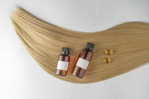 en hår vård olja eller serum i brun dropper flaskor och gyllene kapslar liggande på en blond hår strå, produkt marknadsföring attrapp foto
