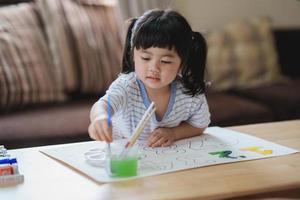 söt liten asiatisk bebis leende målning med färgrik målarfärger använder sig av vattenfärg. asiatisk flicka använder sig av paintbrush teckning Färg. bebis aktivitet livsstil begrepp. foto