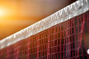 gräddvit badmintonfjärdeboll och racket med neonljusskuggning på grönt golv i inomhusbadmintonbana, suddig badmintonbakgrund, kopieringsutrymme. foto