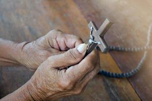 närbild trä- korsa som har en metall staty av korsfäst Jesus är i de händer av ett asiatisk eldery katolik medan bön- i en lokal- kyrka, mjuk och selektiv fokus. foto