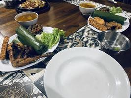 indonesiska kök eller Sundanesiska mat kallad nasi timbel, ris insvept i banan löv, eras med friterad kyckling, tempeh, tofu, saltade fisk, chili sås, lalap och sayur asem. foto