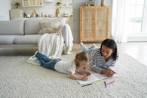 mamma eller barnvakt och liten preschooler unge flicka dotter målning tillsammans liggande på golv matta foto