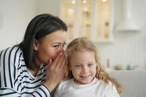 mamma eller barnvakt viska hemlighet till liten elementärt unge flicka dotter. familj enhet, barn vård foto