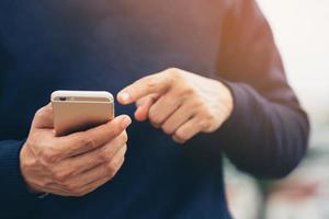 ung man bär rutig skjorta. närbild hand med på mobiltelefon under vila på soffan. sitter och tittar på meddelandet på mobiltelefonen under pausen, slappna av. mjukt fokus. foto